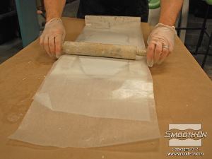 לחיצה להגדלת תמונה מניחים חתיכה נוספת של נייר שעווה על הבצק ומתחילים לרדד אותו בעזרת המארוך לקבלת עובי אחיד.