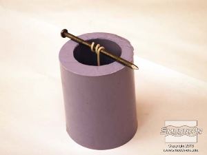 לחיצה להגדלת תמונה מניחים את בסיס הפתיל, הטבול בשעווה, בתחתית תבנית הסיליקון OOMOO® 30. מסדרים את המסמר על התבנית כך שהפתיל יהיה ממורכז.